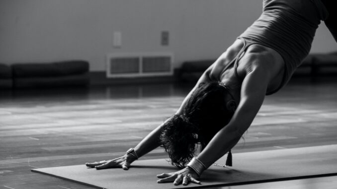 woman in black tank top and black pants bending her body on floor